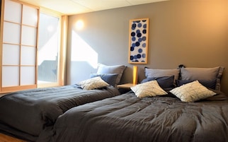 Un dormitorio con dos camas, un separador shoji, una obra de arte colgada en la pared y una mesita de noche con lámpara.