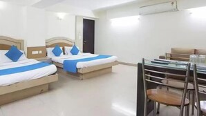 A hotel room with two beds, a dining table with chairs, and an air conditioning unit on the wall. - Hotel Metro Express (New Delhi)