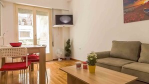 A living room with a wooden coffee table, a sofa, a TV mounted on the wall, and a dining area with chairs and a table. - Dervenion-Athens Cozy Apartment (Athens)