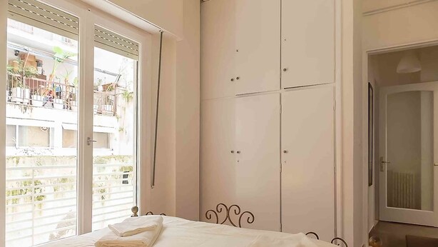A bedroom with a bed, a wardrobe, and a balcony with a view of buildings. - Dervenion-Athens Cozy Apartment (Athens)