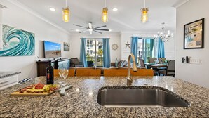 A modern kitchen with granite countertops, a stainless steel sink, and a dining area with blue curtains and a chandelier. - Pet Friendly | Private Pool | Walk to Beach | Lagoon Views (Hilton Head Island)