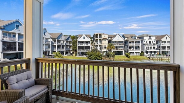 A wooden deck with wicker furniture overlooking a body of water and a row of beachfront houses. - Pet Friendly | Private Pool | Walk to Beach | Lagoon Views (Hilton Head Island)