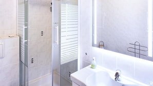 A modern bathroom with a glass-enclosed shower, a white sink, and a large mirror. - Ring Hotel (Wiesbaden)