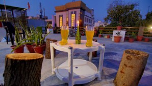 A round table with two glasses of yellow beverage and a lit candle, surrounded by potted plants and a wooden stump. - The Hideout Agra Homestay (Agra)