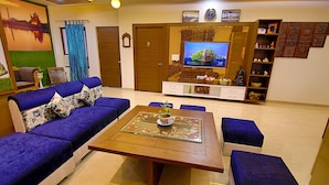 A living room with a sofa set, a coffee table, a television, and a bookshelf. - The Hideout Agra Homestay (Agra)