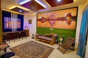 A living room with a sofa, a coffee table, a patterned rug, a ceiling fan, and a wall-mounted TV.