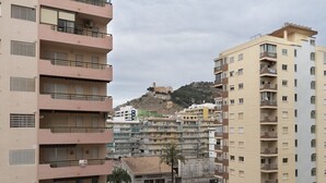Un immeuble résidentiel à plusieurs étages, doté de balcons, donnant sur une rue et situé devant une colline sur laquelle se trouve un fort.