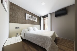 A modern bedroom with a bed, a flat-screen TV, a painting, and a window with blinds. - Hostal Residencia Victoria (Vedra)