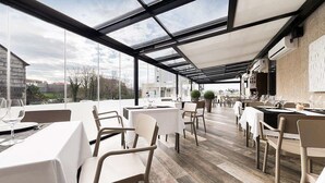Ein Restaurant mit Außenbereich, überdacht durch eine Glasdachkonstruktion, und mit gedeckten Tischen.