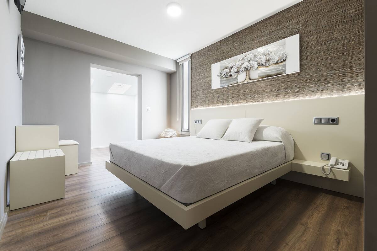 A modern bedroom with a bed, bedside table, and a wall-mounted phone.