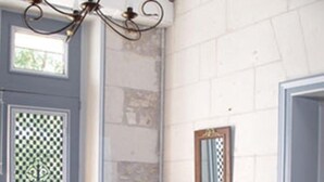 Una habitación con piso a cuadros, un banco de madera con macetas de cerámica, un espejo en la pared y una ventana con un panel decorativo.