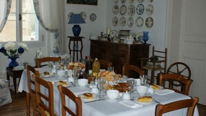 Comedor con una mesa dispuesta para seis personas, rodeada de sillas de madera. Un candelabro cuelga del techo, y una colección de platos se exhibe en la pared.
