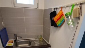 Uma cozinha pequena com janela, pia e armários. Há produtos de limpeza pendurados na parede.