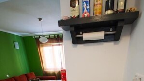 Uma cozinha compacta com forno embutido, micro-ondas e cafeteira. Há uma prateleira sobre a bancada com diversos frascos.