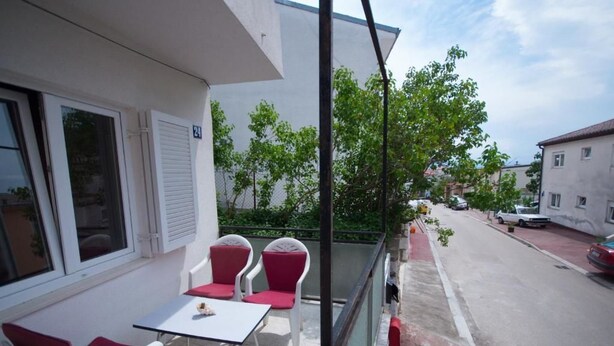 Varanda com área de estar externa, vista para a rua e um prédio com placa de número.