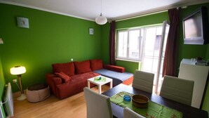 Quarto com paredes verdes, um sofá vermelho, uma mesinha e uma mesa de jantar com cadeiras.