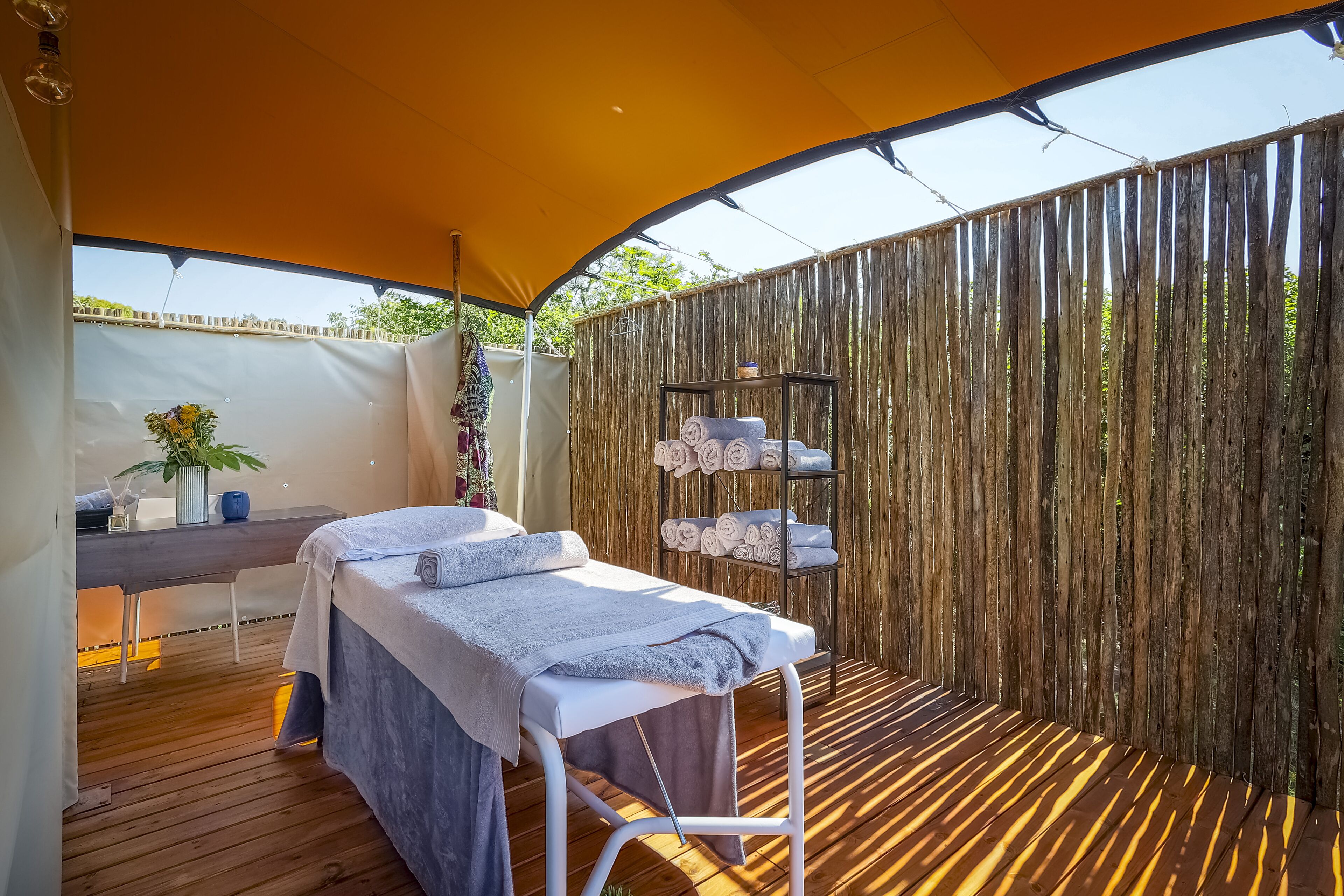 Een wellnessruimte met een massagetafel, een klein bureau met een plant en een plank met handdoeken.
