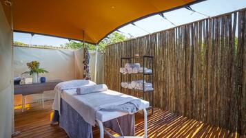 Een wellnessruimte met een massagetafel, een klein bureau met een plant en een plank met handdoeken.
