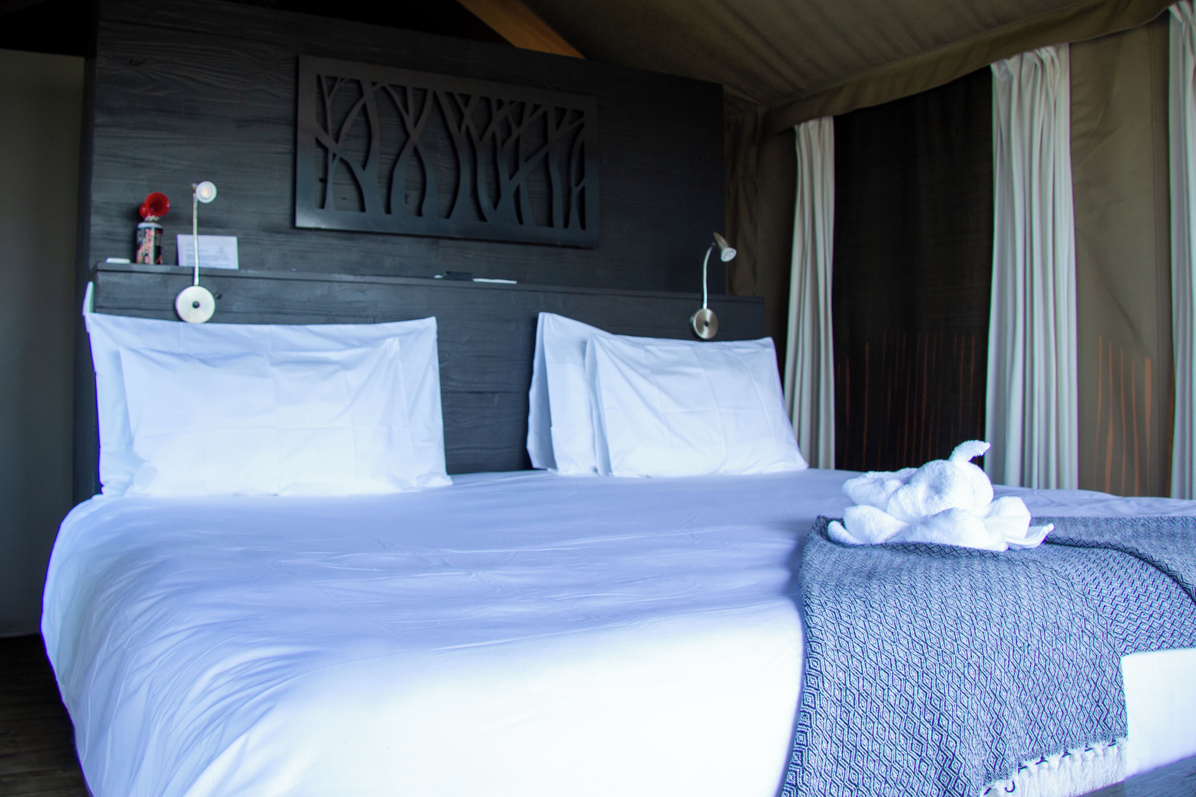 A large bed with white linens, a decorative wall piece, and a towel on the bed.