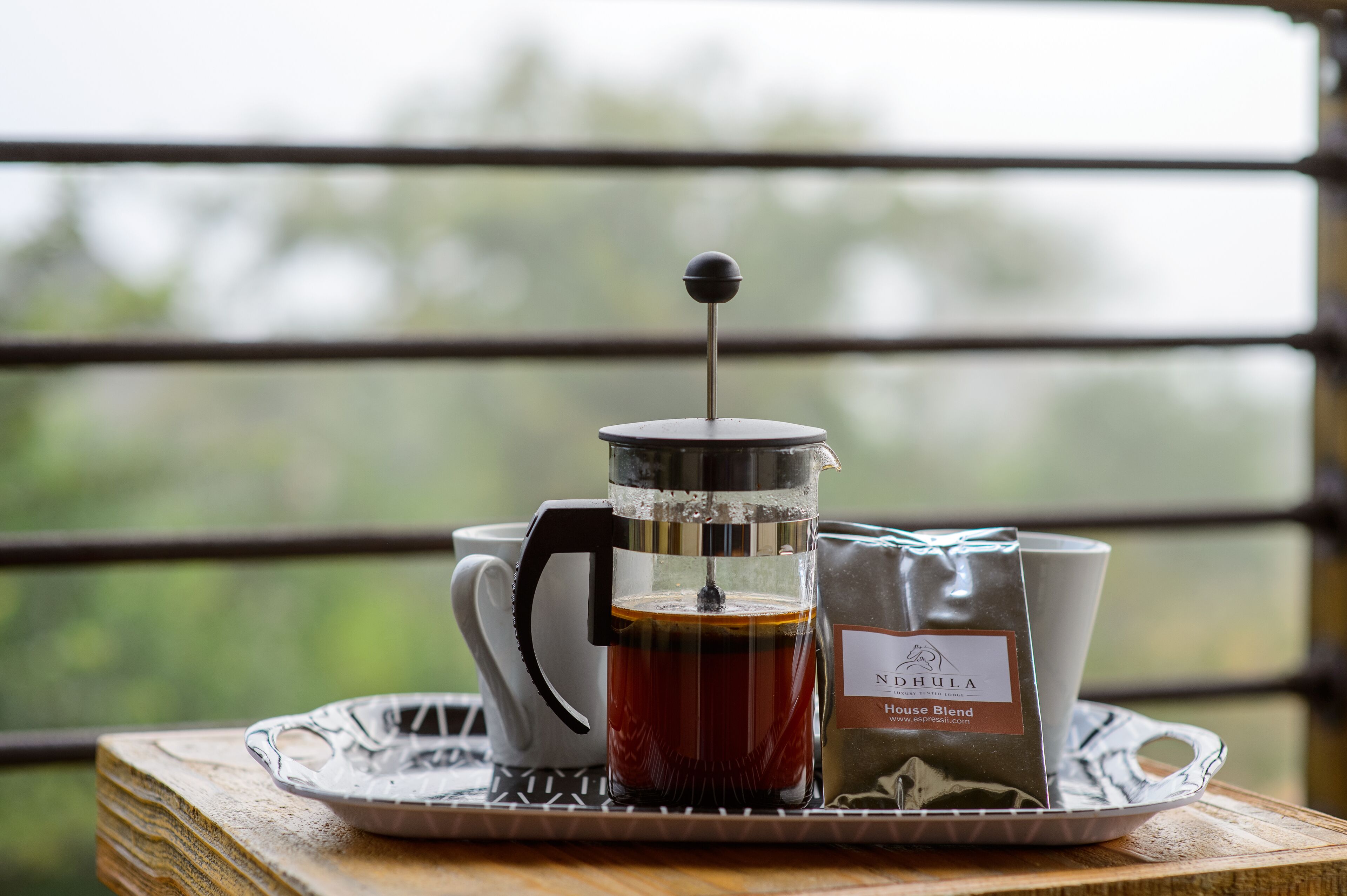 Una cafetera francesa con una bolsa de café y una taza sobre una bandeja.