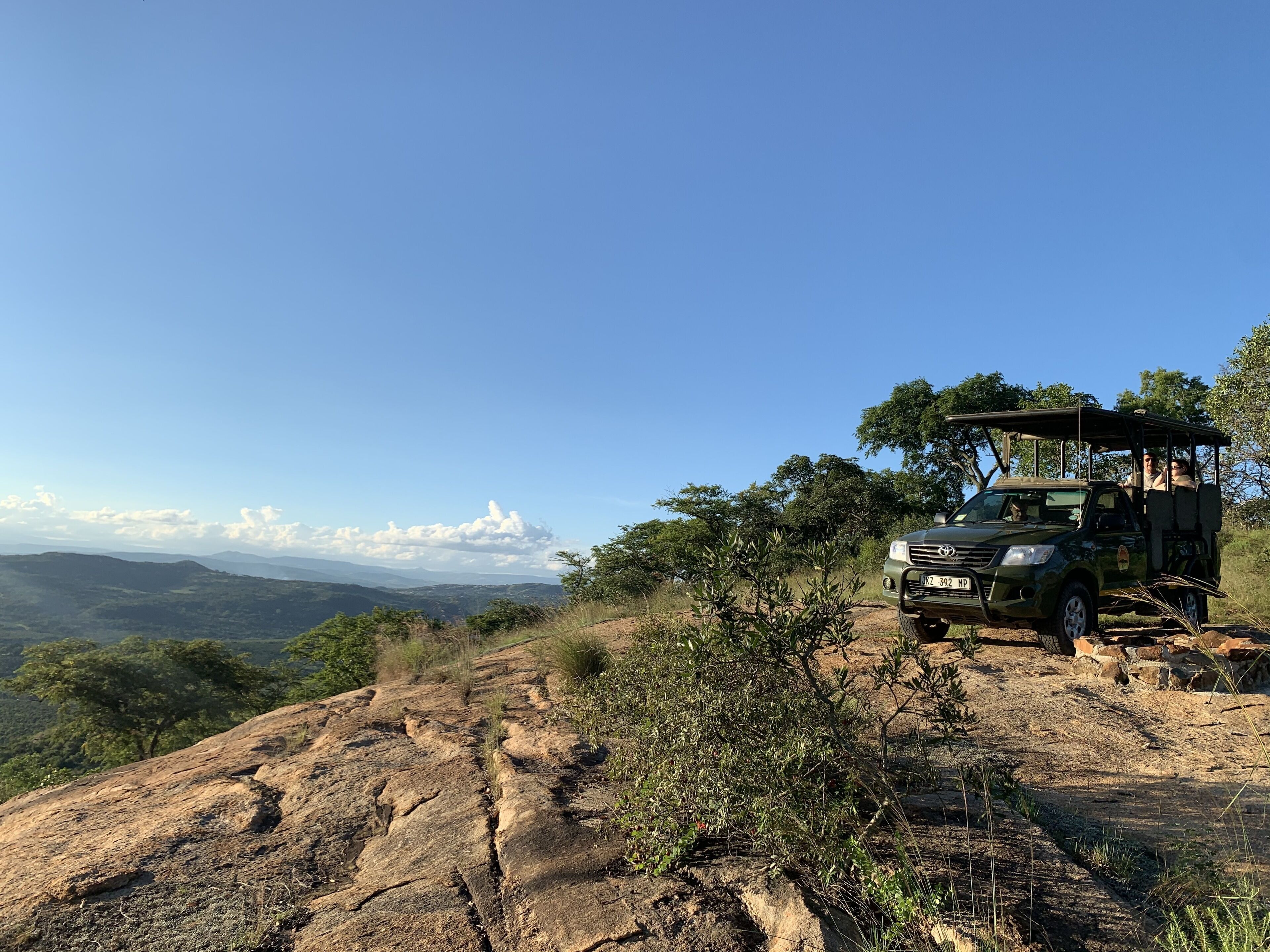 Un vehículo de safari estacionado en un afloramiento rocoso con vistas a montañas distantes y un cielo despejado.