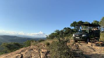 Un vehículo de safari estacionado en un afloramiento rocoso con vistas a montañas distantes y un cielo despejado.