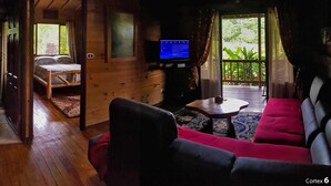 L’intérieur d’un chalet en bois comprend un lit, un téléviseur, un canapé et un balcon offrant une vue sur la verdure.