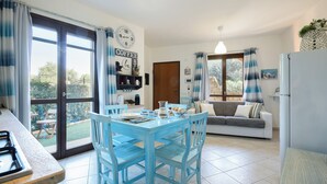 Una cocina con mesa y sillas, un refrigerador, un sofá y una ventana con cortinas.