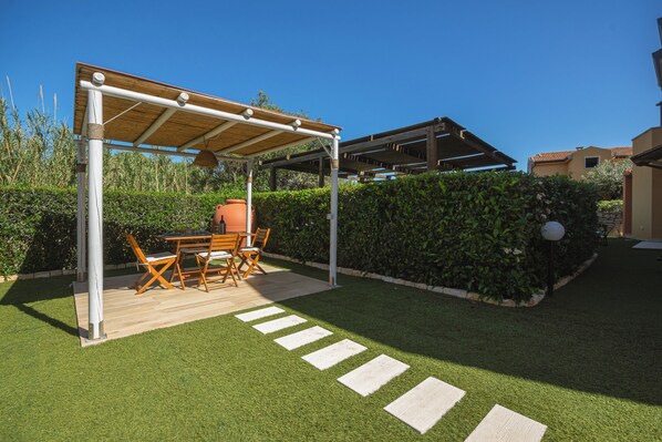 A covered patio with a table and chairs, surrounded by a well-maintained lawn and hedges.