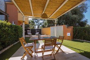 An outdoor patio with a table set for dining, surrounded by chairs, and a covered area with a hanging light fixture.