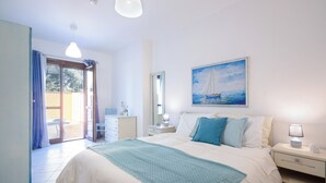 Un dormitorio con cama, mesita de noche, lámpara, un cuadro, un espejo y una puerta corrediza de vidrio que da a un área exterior.
