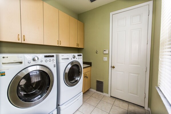 A laundry room with two front-loading washing machines, wooden cabinets, a white door, and a tiled floor. - Stunning Lake View Pool Villa with SPA and Heated Pool<br> (Cape Coral)