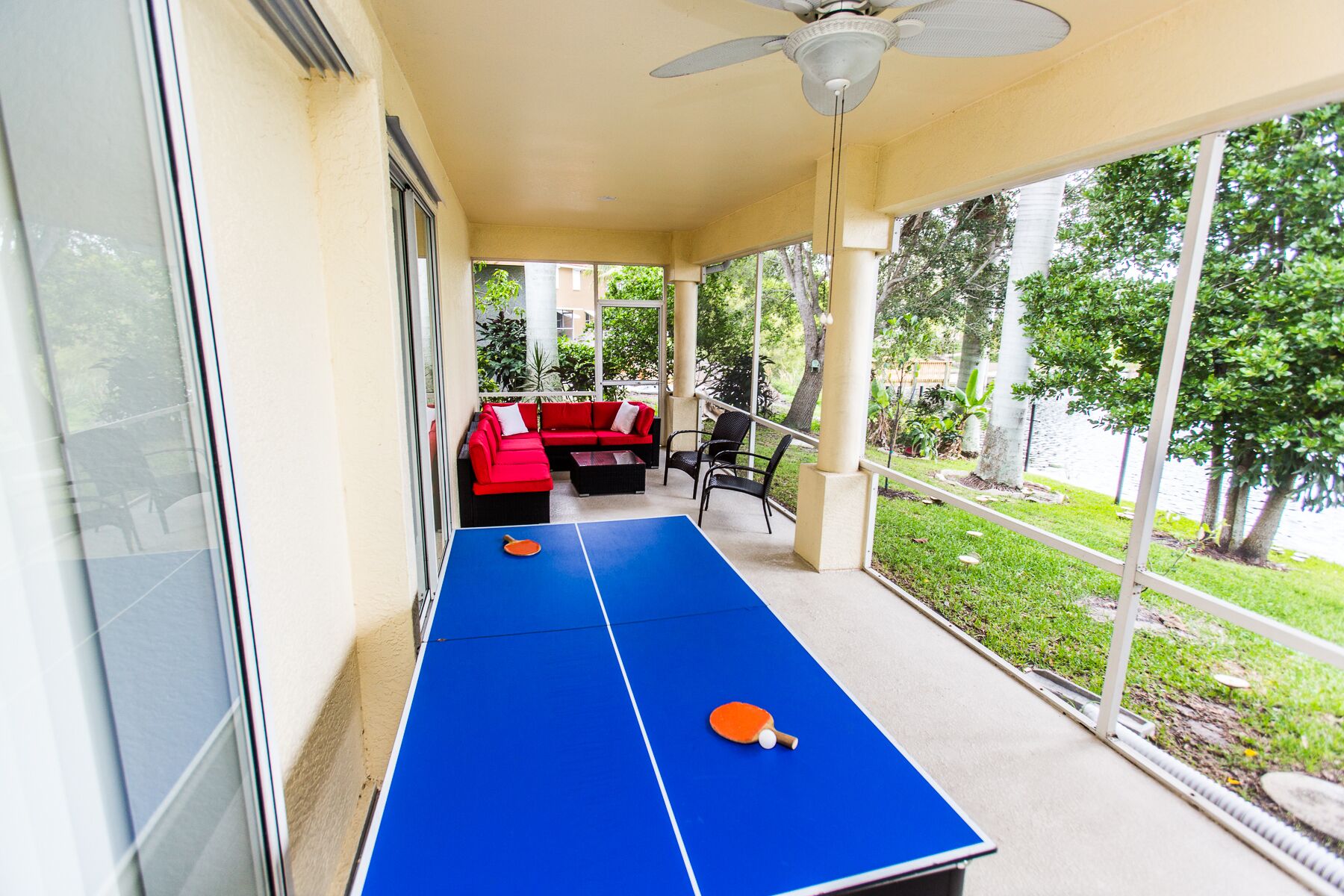 Un espacio exterior techado con mesa de ping pong, asientos rojos y ventilador de techo.