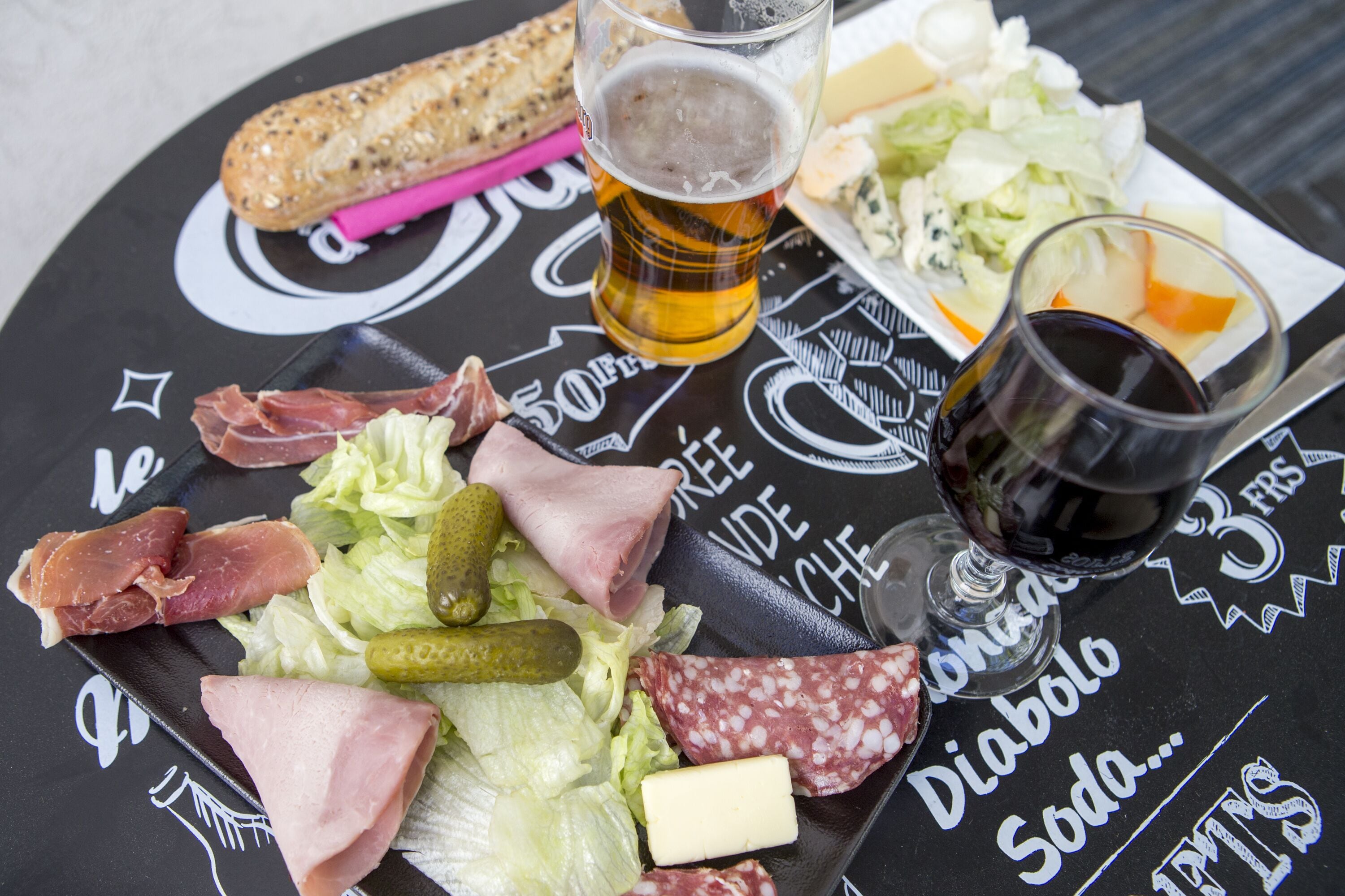 A table with various food items and drinks, including meats, cheese, and a glass of beer.
