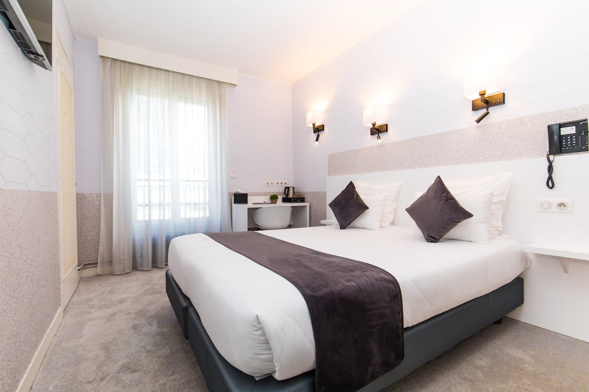 Une chambre d’hôtel avec un grand lit, un bureau avec une chaise, une machine à café et un téléphone fixé au mur.