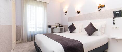 A hotel room with a large bed, a desk with a chair, a coffee maker, and a phone on the wall.