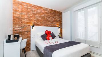 Una habitación de hotel con una pared de ladrillo decorativa, una cama con colcha blanco y gris, un escritorio con tetera y una silla.