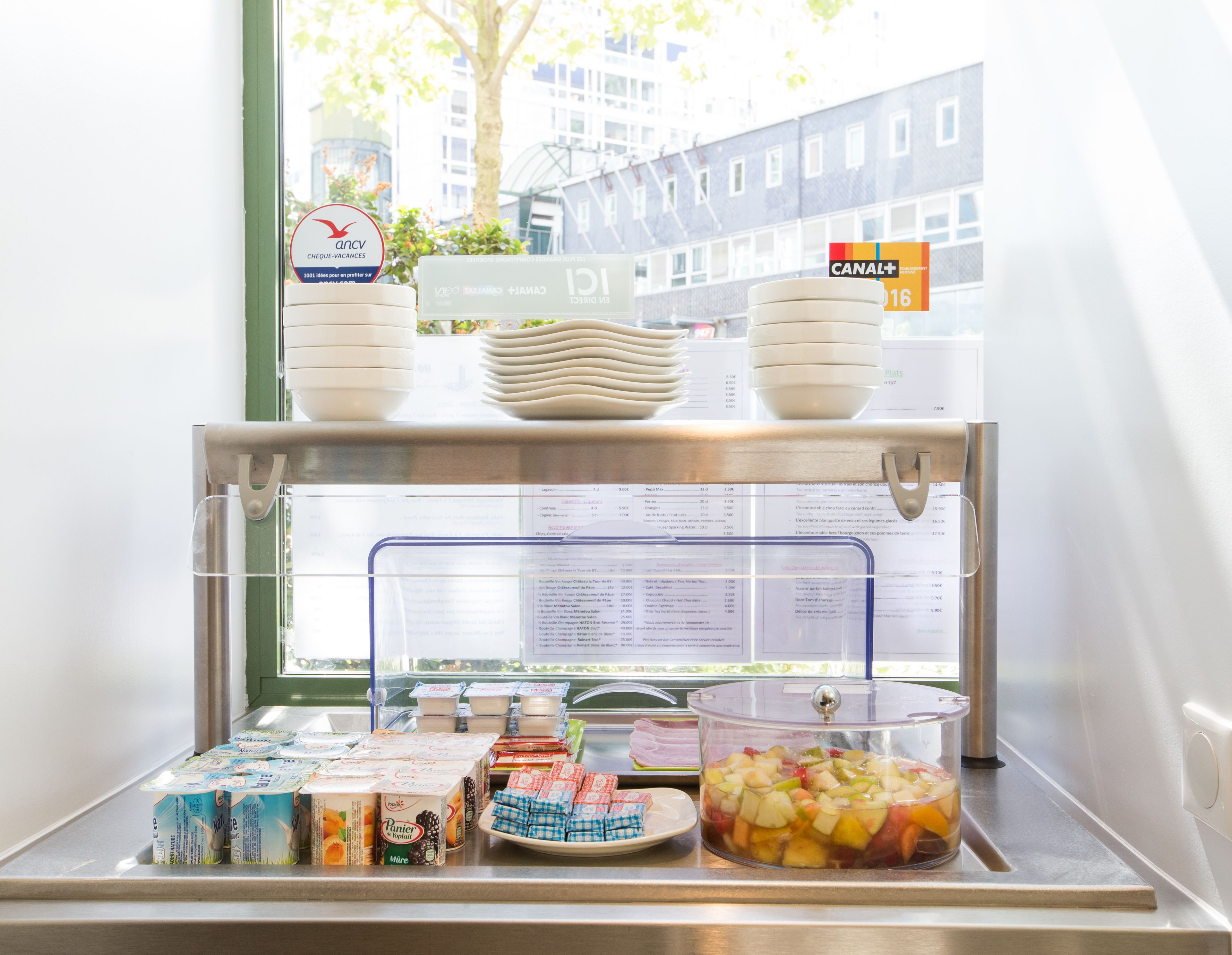 A breakfast buffet with various food items and containers, including yogurt, cereal, and a fruit salad.