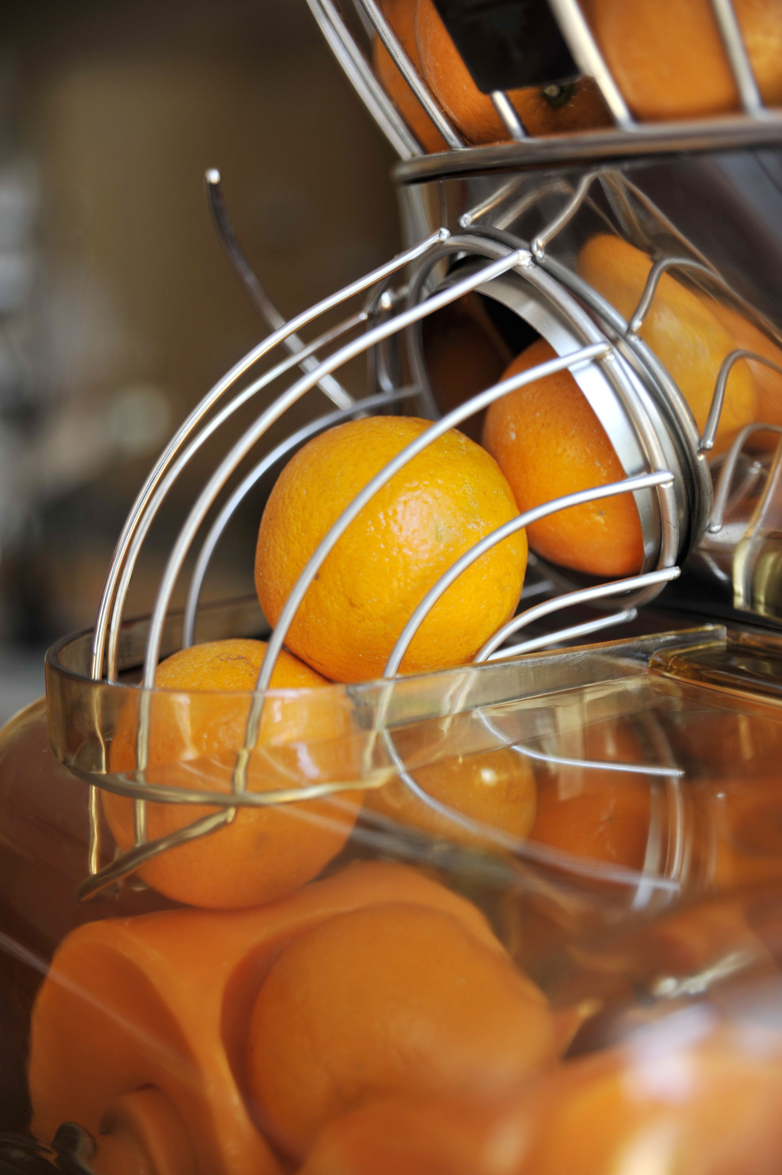 A metal fruit basket with oranges inside a glass container.