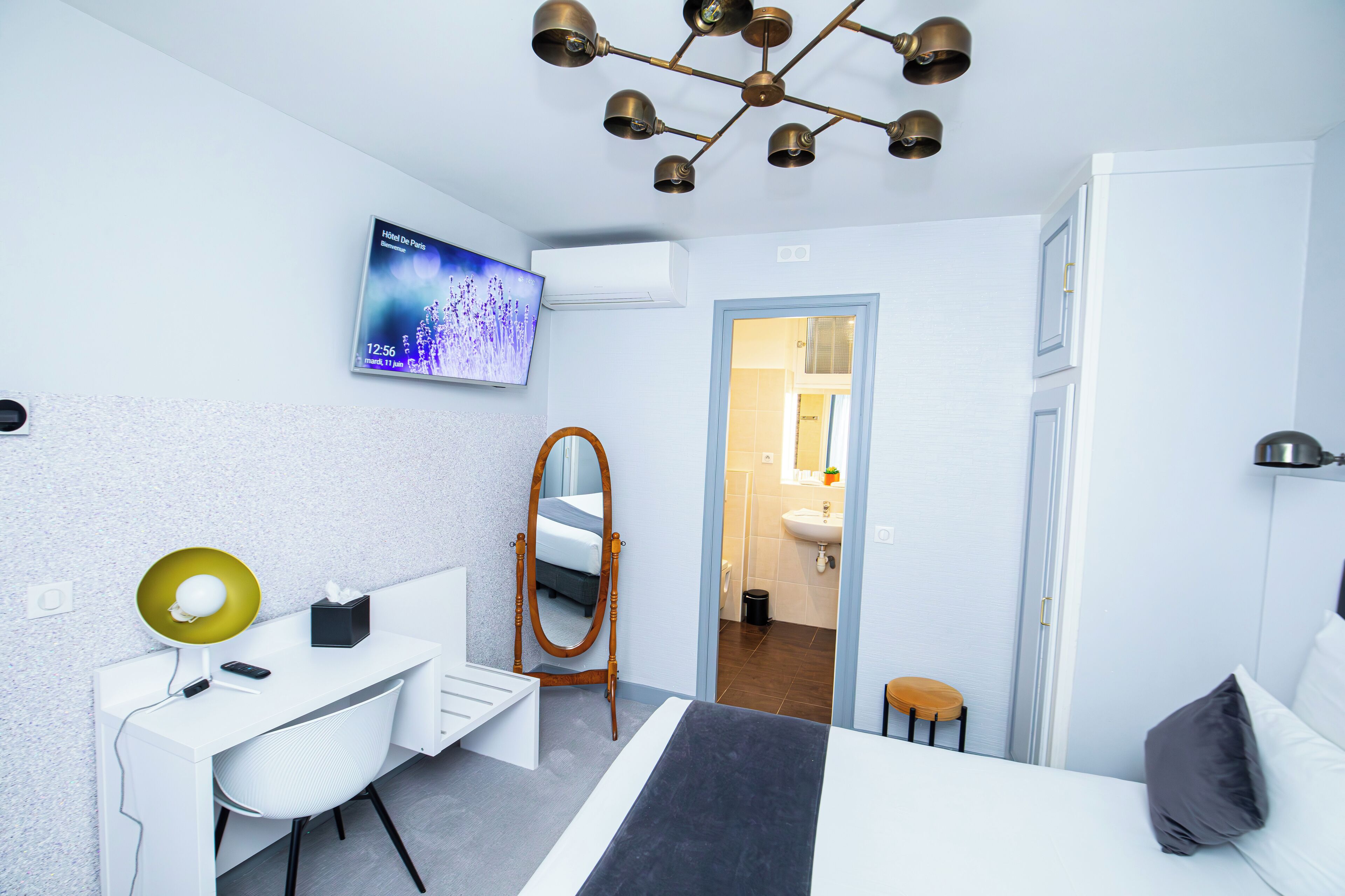 A modern hotel room with a desk, chair, bed, and a TV mounted on the wall.