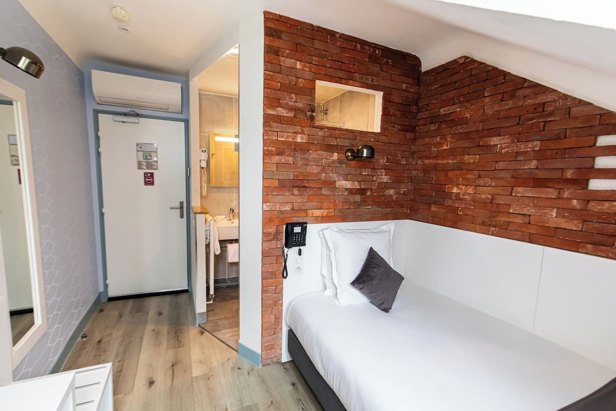 Une chambre d’hôtel avec un mur d’accent en briques, un lit blanc, un petit miroir et un téléphone fixé au mur.