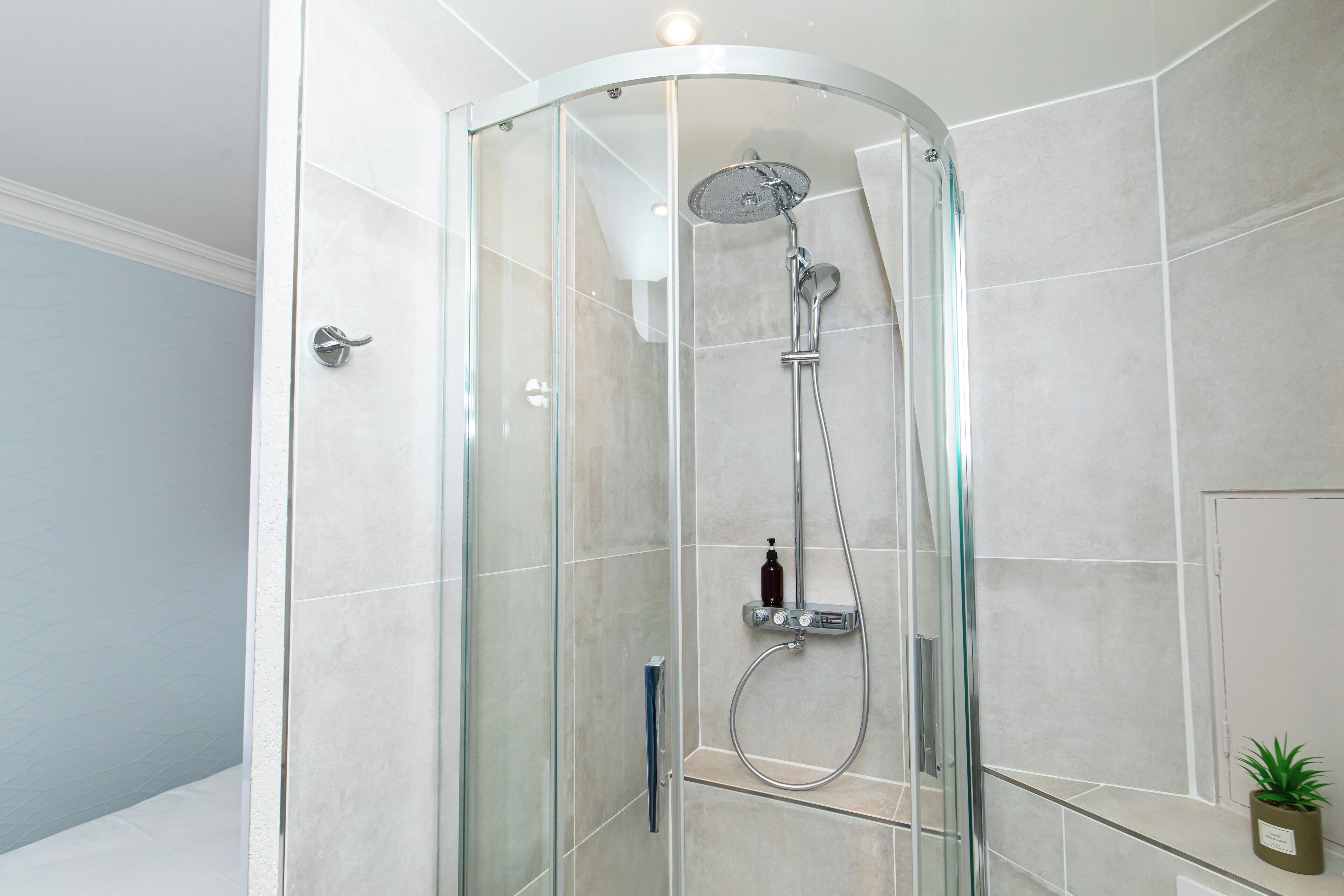 A glass-enclosed shower with a handheld showerhead and a wall-mounted faucet.