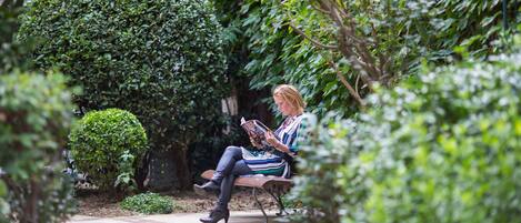 A person sitting on a bench in a garden with well-maintained bushes and a clear pathway.
