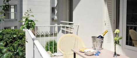 Ein Balkon mit weißem Stuhl, einem Tisch mit einer Champagnerflasche und einer Vase mit Blumen.