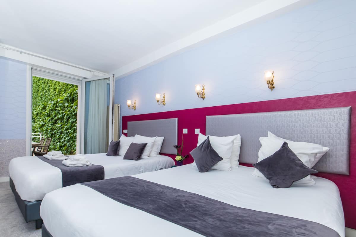 Une chambre d’hôtel avec deux lits, une grande fenêtre donnant sur un paysage verdoyant et un mur d’accent de couleur rose.