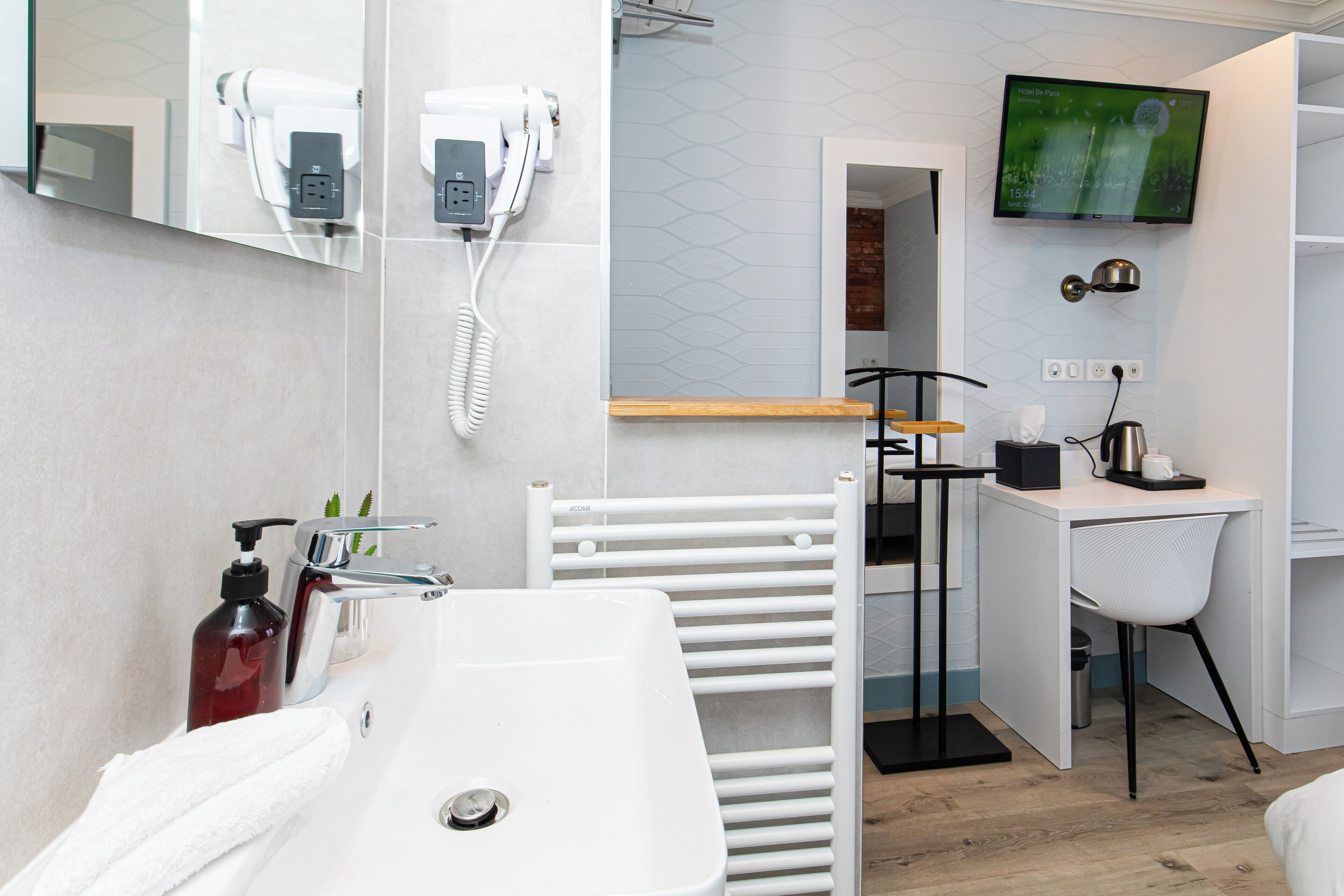 Un baño moderno con lavamanos blanco, toallero, secador de pelo y televisor montado.