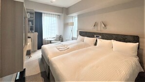 Una habitación de hotel con dos camas, un escritorio, una silla, una lámpara y una ventana.