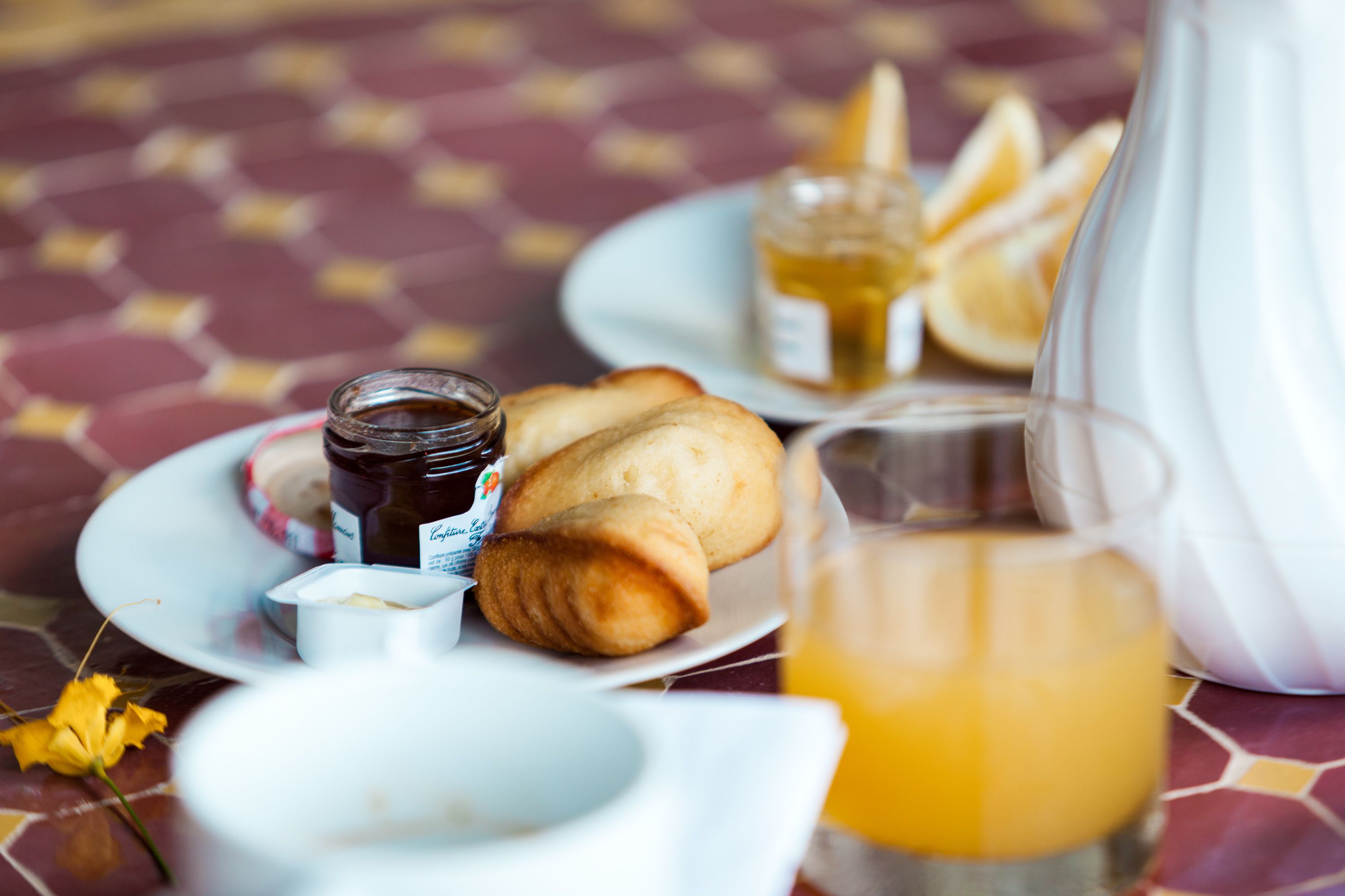 A breakfast setting with pastries, honey, and orange juice on a patterned tablecloth.