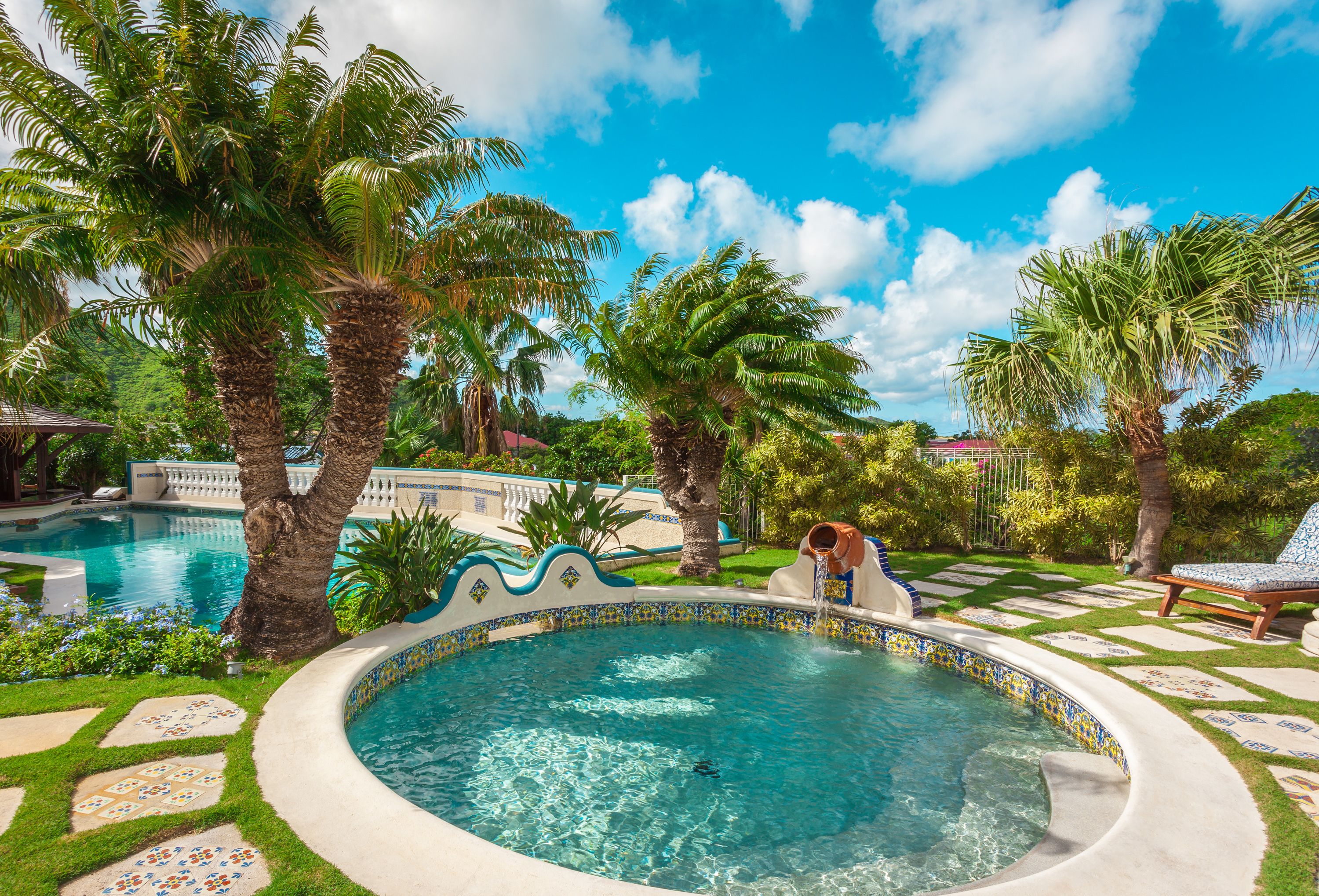 A swimming pool with a tiled edge, surrounded by palm trees and a well-maintained lawn.