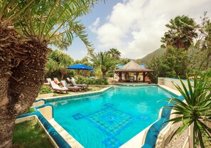 A swimming pool with lounge chairs and umbrellas, surrounded by palm trees and a gazebo. - Hotel L'Esplanade (Grand Case)